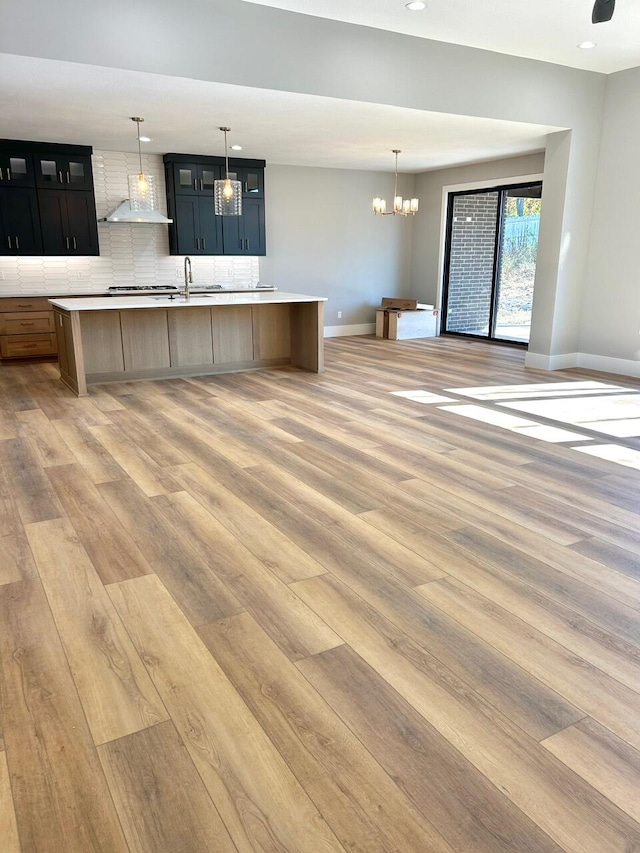 kitchen featuring backsplash, a kitchen island with sink, light hardwood / wood-style flooring, wall chimney exhaust hood, and a notable chandelier