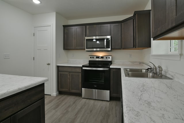 kitchen with appliances with stainless steel finishes, dark brown cabinets, sink, and light hardwood / wood-style flooring