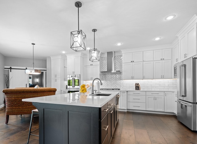 kitchen with white cabinets, sink, a center island with sink, wall chimney range hood, and appliances with stainless steel finishes