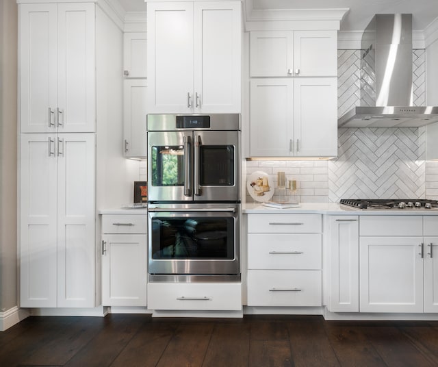 kitchen with wall chimney exhaust hood, white cabinetry, and stainless steel appliances