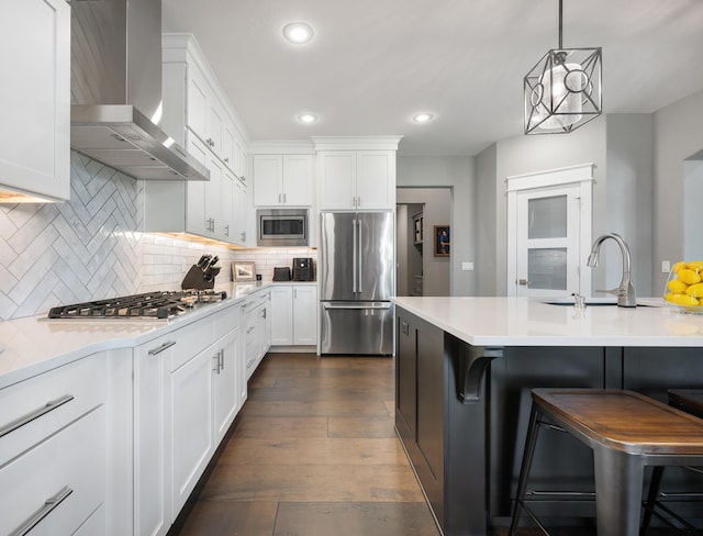 kitchen featuring a kitchen bar, wall chimney range hood, white cabinets, and built in appliances