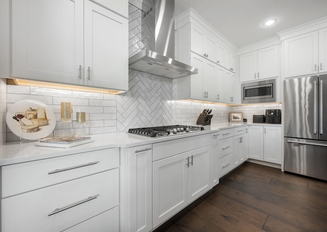 kitchen featuring dark hardwood / wood-style floors, white cabinets, wall chimney range hood, appliances with stainless steel finishes, and backsplash