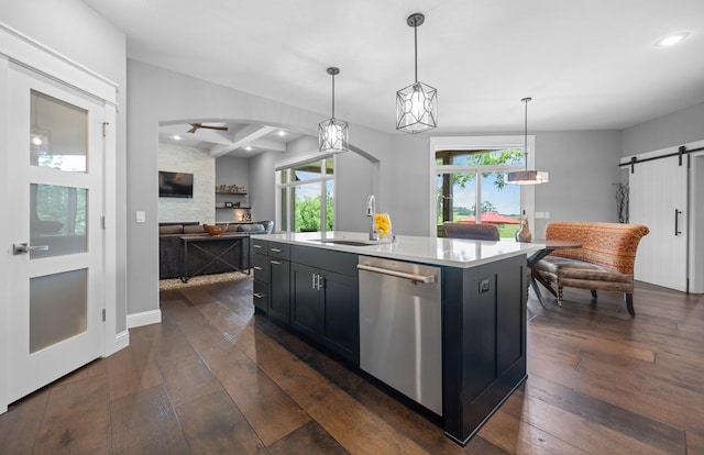 kitchen featuring a barn door, dark wood-type flooring, hanging light fixtures, an island with sink, and stainless steel dishwasher