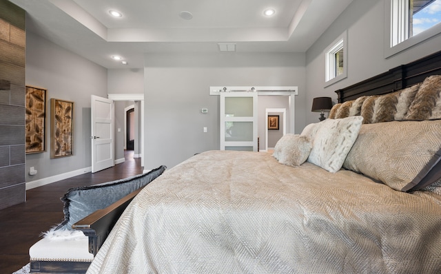 bedroom with a raised ceiling, a barn door, dark wood-type flooring, and multiple windows