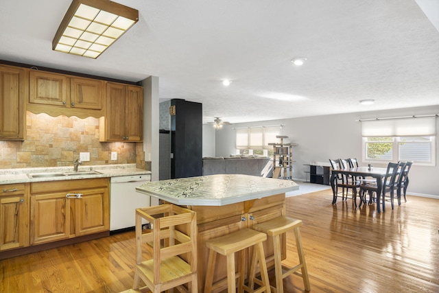 kitchen with a breakfast bar area, light hardwood / wood-style flooring, sink, white dishwasher, and backsplash