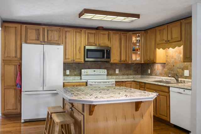 kitchen featuring a kitchen island, dark hardwood / wood-style floors, a breakfast bar, white appliances, and sink