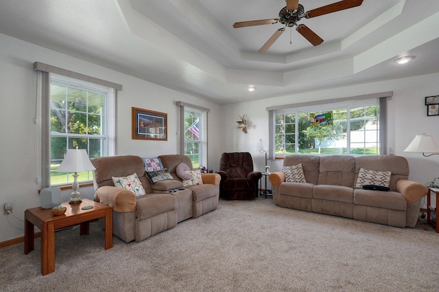 carpeted living room with ceiling fan, plenty of natural light, and a tray ceiling