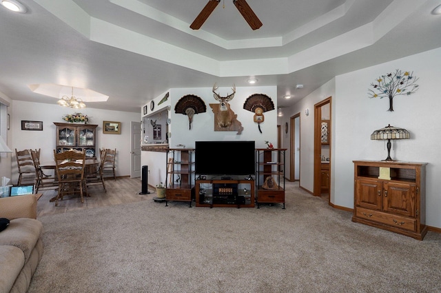 living room featuring a raised ceiling, ceiling fan with notable chandelier, and carpet floors