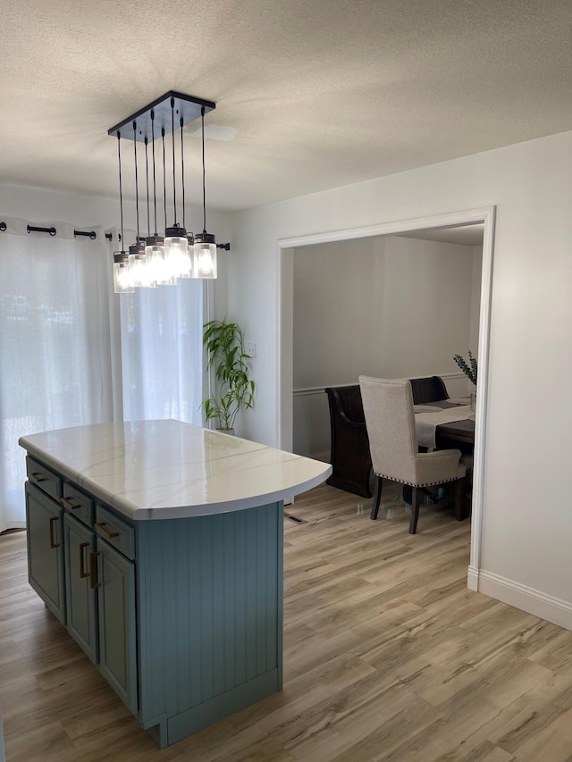 kitchen featuring light hardwood / wood-style floors, decorative light fixtures, light stone countertops, a center island, and a textured ceiling