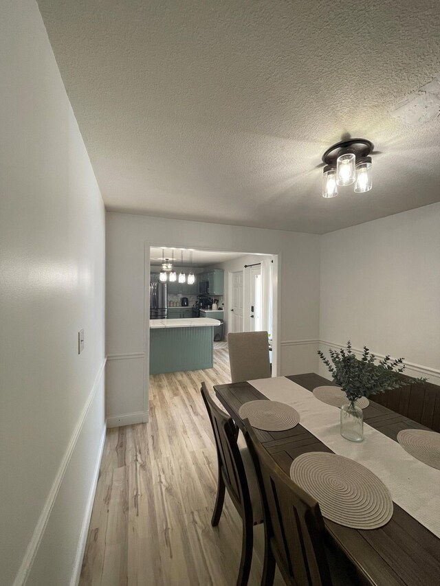 dining area featuring light wood-type flooring and a textured ceiling