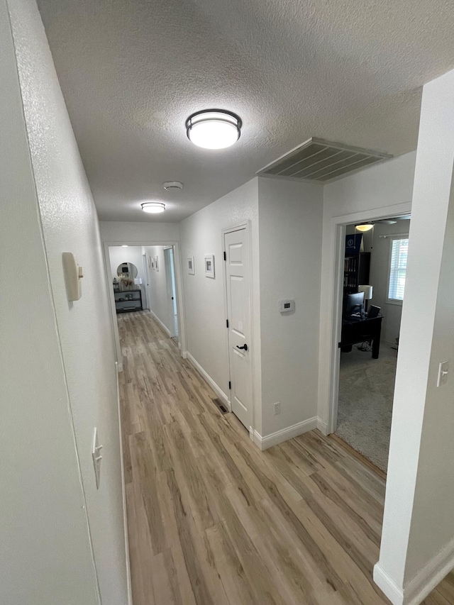 corridor with light hardwood / wood-style floors and a textured ceiling