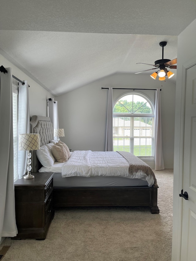 bedroom with lofted ceiling, light colored carpet, a textured ceiling, and ceiling fan