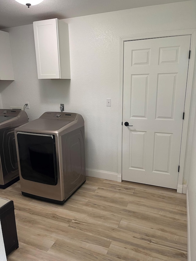 clothes washing area featuring washer and dryer, cabinets, and light wood-type flooring