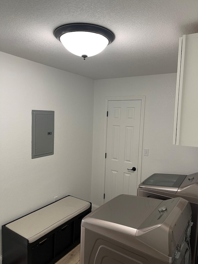 laundry room with electric panel, a textured ceiling, light hardwood / wood-style floors, and washing machine and clothes dryer