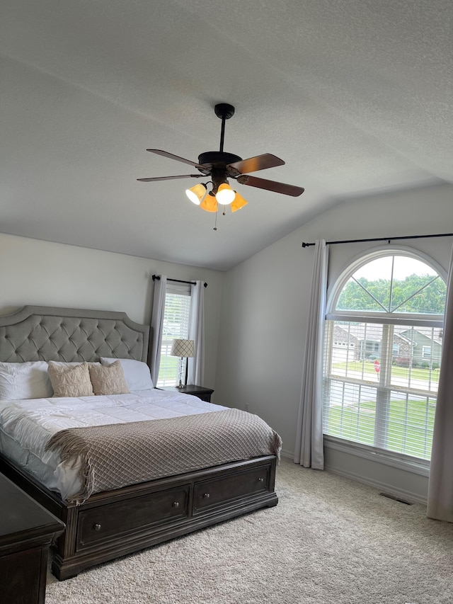 carpeted bedroom featuring ceiling fan, a textured ceiling, vaulted ceiling, and multiple windows