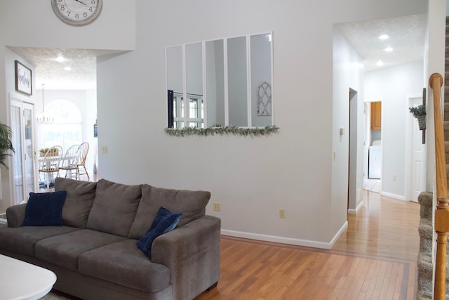 living room featuring wood-type flooring, a textured ceiling, an inviting chandelier, and washer / dryer