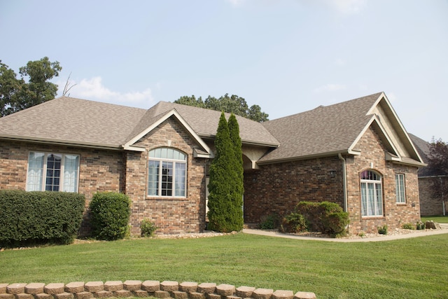 ranch-style house with roof with shingles, a front yard, and brick siding