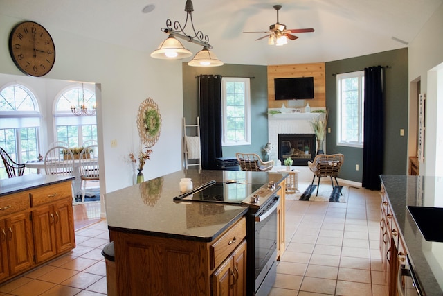 kitchen with ceiling fan with notable chandelier, stainless steel range with electric cooktop, open floor plan, light tile patterned floors, and a brick fireplace