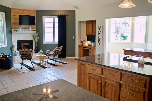 kitchen featuring dark stone counters, a brick fireplace, brown cabinets, and light tile patterned floors
