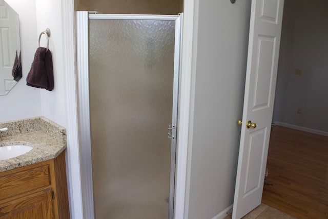 full bathroom with baseboards, wood finished floors, vanity, and a shower stall