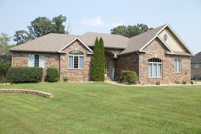 view of front of home featuring a shingled roof, brick siding, and a front yard