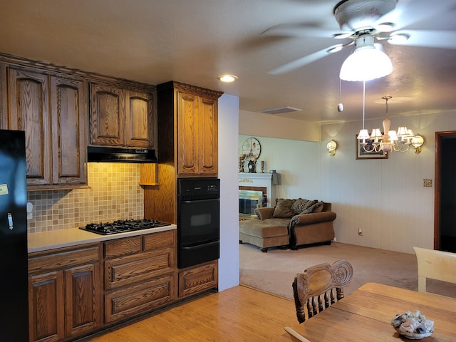 kitchen featuring light hardwood / wood-style floors, tasteful backsplash, ceiling fan with notable chandelier, decorative light fixtures, and black appliances