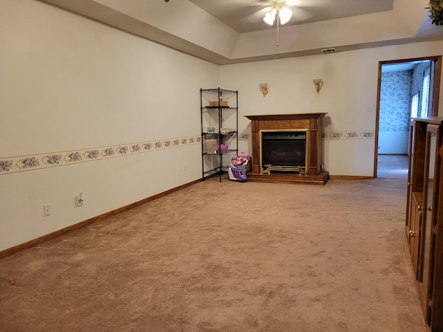 unfurnished living room with ceiling fan, a tray ceiling, and carpet flooring