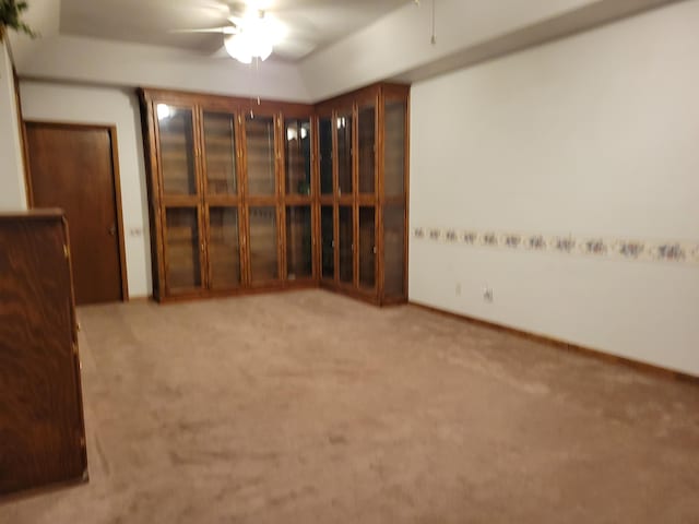 empty room featuring ceiling fan, light colored carpet, and a raised ceiling