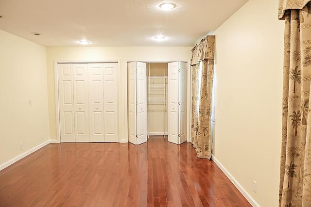 unfurnished bedroom featuring baseboards, multiple closets, wood finished floors, and recessed lighting