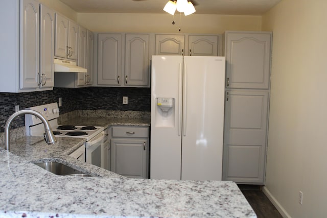 kitchen with white appliances, tasteful backsplash, light stone countertops, sink, and dark wood-type flooring