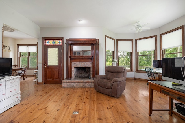 living room featuring ceiling fan, light hardwood / wood-style floors, and a brick fireplace