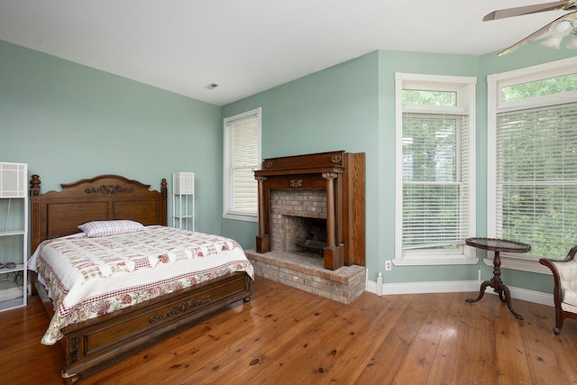 bedroom featuring ceiling fan, wood-type flooring, and a brick fireplace