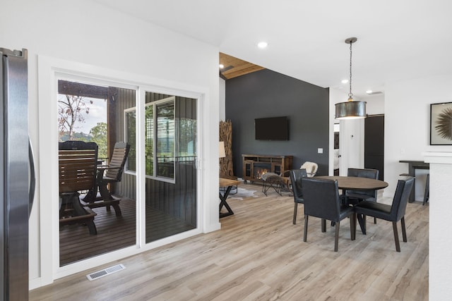 dining area featuring lofted ceiling, recessed lighting, visible vents, light wood-style flooring, and a lit fireplace