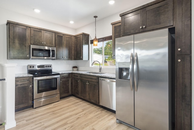 kitchen with light stone counters, appliances with stainless steel finishes, light wood-style floors, a sink, and dark brown cabinets