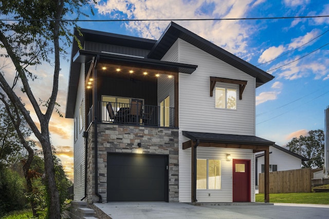 contemporary home featuring a balcony, stone siding, an attached garage, fence, and board and batten siding