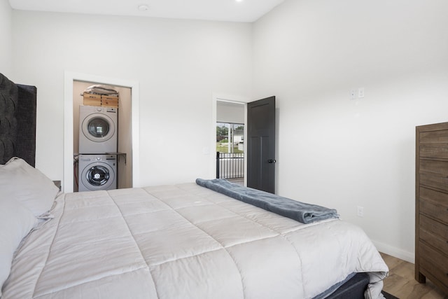 bedroom with stacked washing maching and dryer, wood finished floors, and a towering ceiling