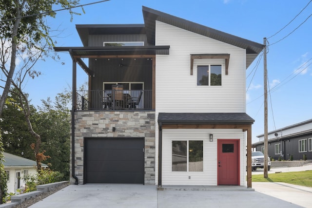 modern home featuring an attached garage, stone siding, a balcony, and concrete driveway