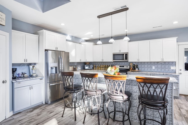 kitchen featuring hanging light fixtures, stainless steel appliances, a kitchen breakfast bar, light hardwood / wood-style floors, and white cabinets