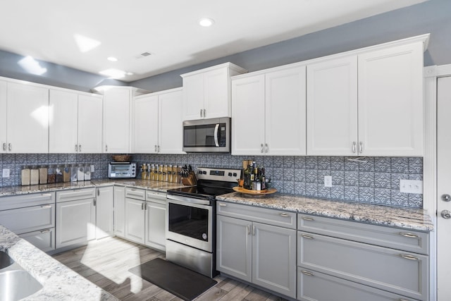 kitchen with appliances with stainless steel finishes, light hardwood / wood-style floors, white cabinetry, and tasteful backsplash