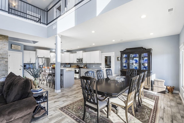 dining room with decorative columns, a towering ceiling, and light hardwood / wood-style floors