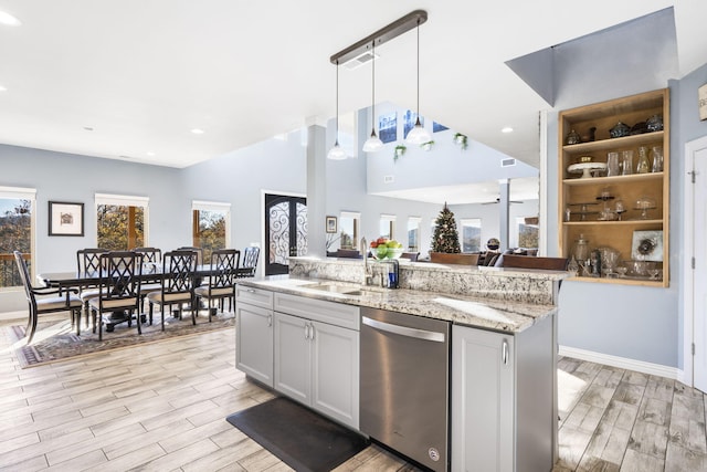 kitchen with light wood-type flooring, stainless steel dishwasher, sink, decorative light fixtures, and a center island with sink