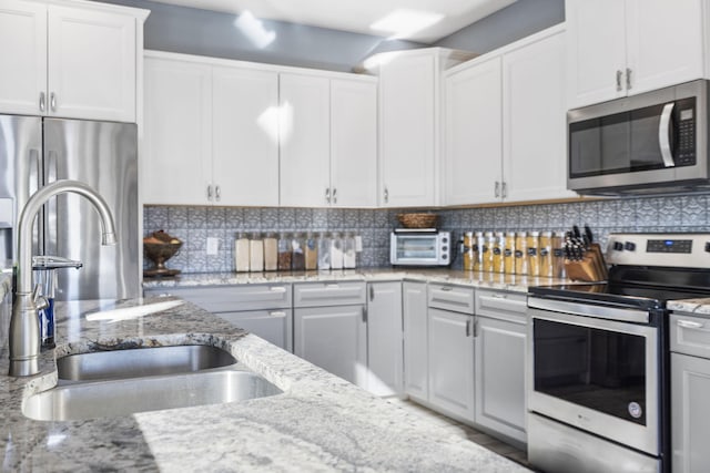 kitchen featuring white cabinets, appliances with stainless steel finishes, backsplash, and light stone counters