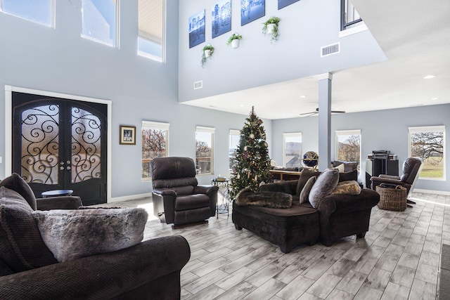 living room featuring ceiling fan, a healthy amount of sunlight, a towering ceiling, and light hardwood / wood-style flooring