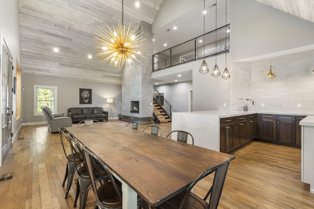 dining area with light wood-type flooring, wooden ceiling, high vaulted ceiling, and a large fireplace