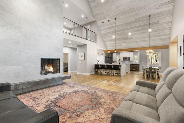 living room with high vaulted ceiling, a fireplace, and light hardwood / wood-style floors