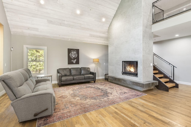 living room featuring light hardwood / wood-style flooring, a tiled fireplace, wood ceiling, and high vaulted ceiling