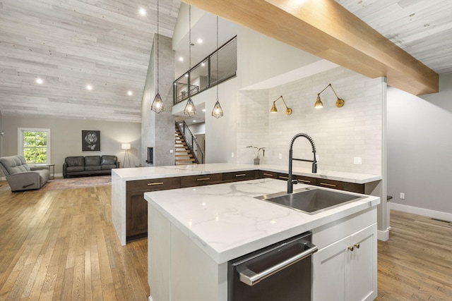 kitchen featuring dishwasher, light stone countertops, white cabinets, and a center island with sink