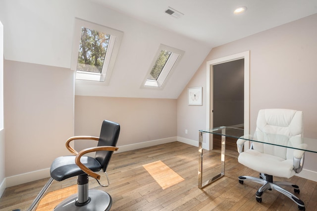 office area with vaulted ceiling with skylight and light hardwood / wood-style floors