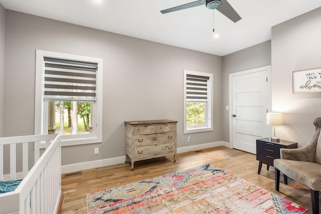 bedroom with ceiling fan, light wood-type flooring, multiple windows, and a crib