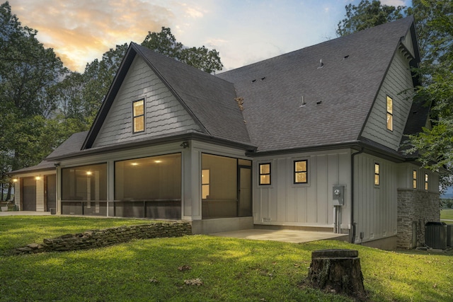 back house at dusk with a yard, a sunroom, and central AC unit